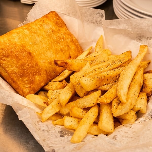 Golden-brown fried fish and seasoned french fries served in a paper-lined basket on a metal counter.