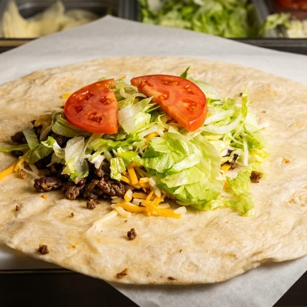 A large tortilla filled with seasoned ground beef, shredded lettuce, cheese, and two tomato slices.