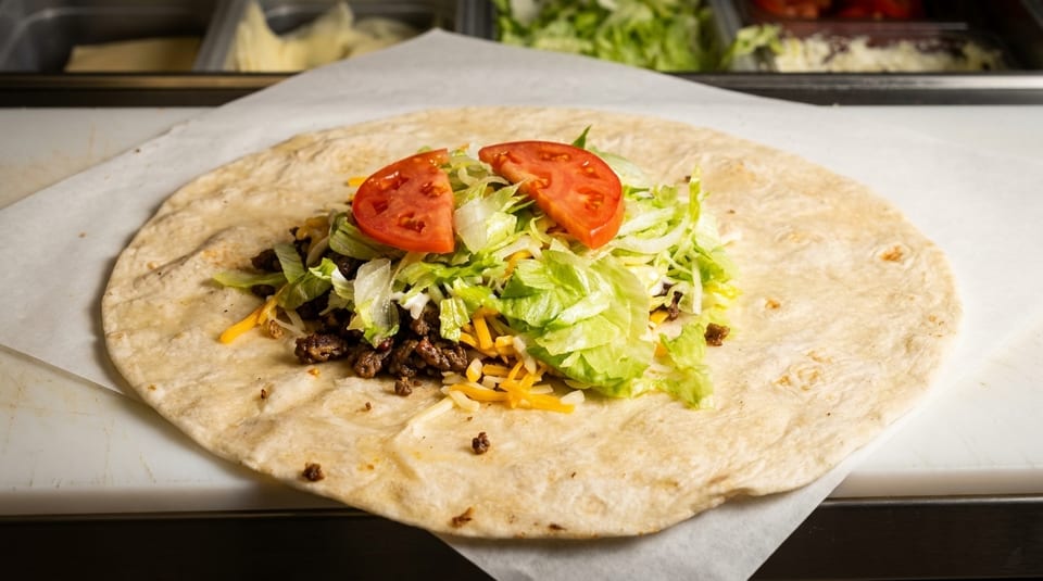 A large tortilla filled with seasoned ground beef, shredded lettuce, cheese, and two tomato slices.